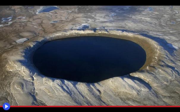 Veduta aerea di cratere da impatto meteoritico perfettamente circolare, in territorio brullo e privo di vegetazione. L'acqua di un profondo azzurro riflette il colore del cielo.