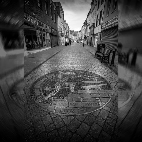 Circular street art done in pebbles of ship, cannon and soldier