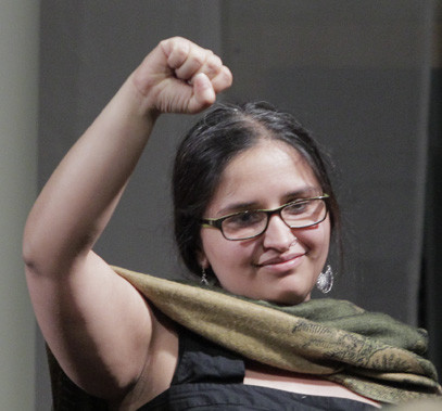 a woman with glasses and an Indian green scarf is raising her right fist and smiling - Harsha-Walia for CCPA-Youth-Awards, 2014