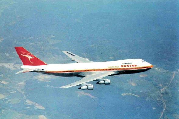 The big jet is flying high. We are looking down on it. It is flying left to right. This is an early 747 and has the 1970s Qantas livery.