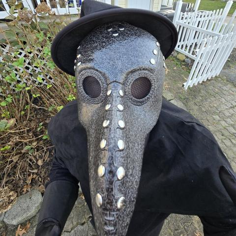 Photograph taken from above of a person in a plague doctor costume. The beak on that mask looks wild and long.