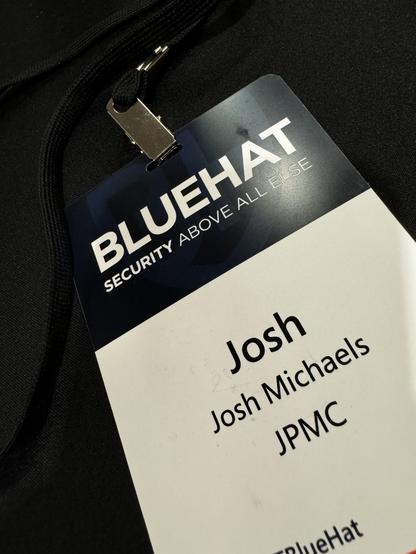 A badge that can be worn around the next for bluehat security conference.  It has the name Josh Michaels and JPMC in the center of a white background. There is a blue rectangle across the top, inside in white text says bluehat security above all else