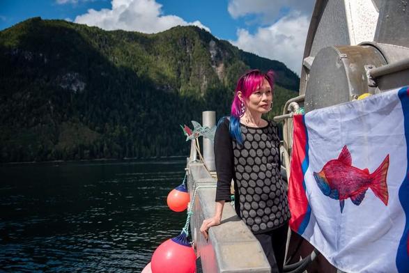Me, standing beside one of our painted wild salmon flags on the side of fishing boat. Ocean & mountains are in the background.