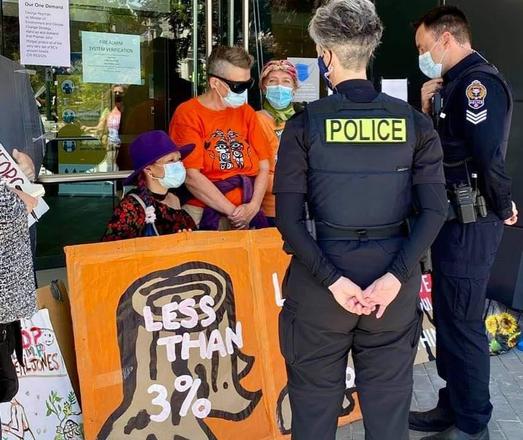 Three of us female activists, locked up & blocking a BC government building. 2 cops are talking to us.