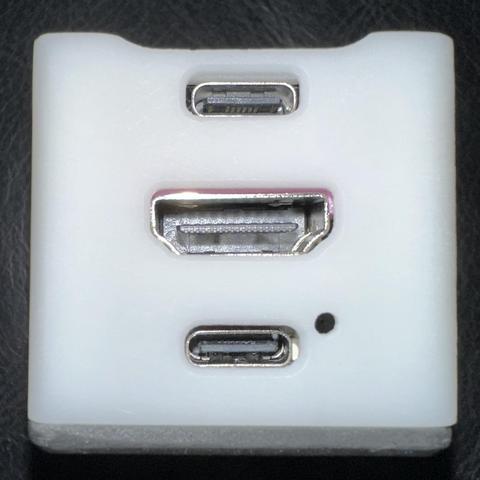 A white square with a central HDMI port between 2 USB-C ports.