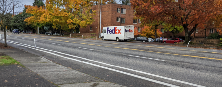 FedEx truck parked in the bike lane and on the sidewalk, plastic posts on some of the paint