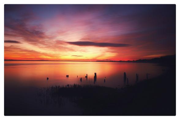A deep red and purple sunset over the river Humber with old post's sticking up out of the river silhouetted by the reflection of the glowing sky