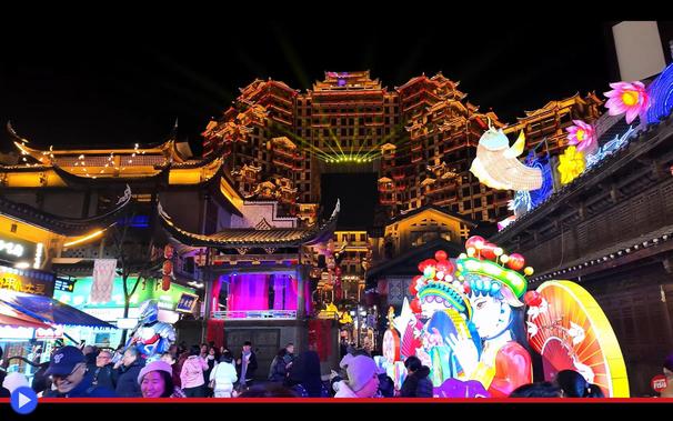 Veduta notturna d'imponente edificio cinese con configurazione architettonica inusuale, in cui due torri laterali sostengono una componente sopraelevata simile a una pagoda. L'illuminazione è caotica e variopinta.