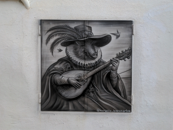 Sur une plaque carrée noire dans un mur blanc, en niveau de gris, un sanglier anthropomorphe assis, habillé comme au XVIe siècle avec un grand manteau, une fraise et un grand chapeau à plumes, joue de la mandoline ; signé "@horacio_bezunartea".