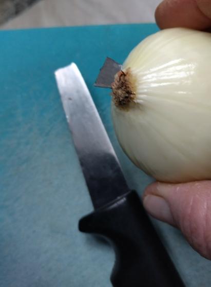 Sinisellä leikkuulaudalla on veitsi, jossa ei ole kärkeä. Se kärki on vieressä sormien välissä olevassa sipulissa kiinni.