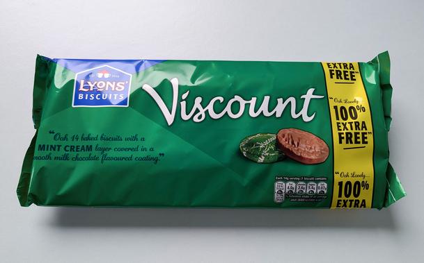 A twin pack of chocolate biscuits are on a white surface. The packaging is a mint green colour with Viscount written large in white over photography of one thick chocolate biscuit unwrapped and one still sealed in metallic green foil. A yellow banner down the right side of the packaging reveals the twin pack has 100% extra free.