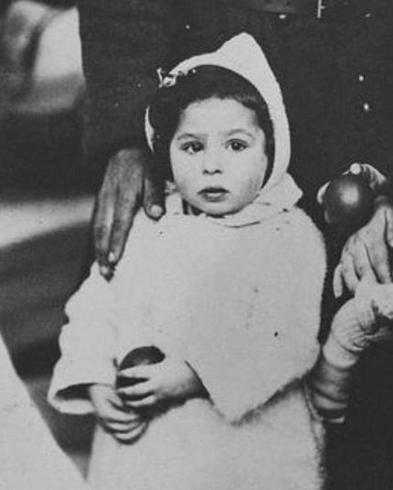 A young girl in white hooded coat holding something in her hands.