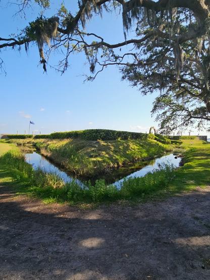 Nearest I was able to manage of capturing the full fort exhibit, including the moat, ancient French flag, hedges, arched entrance, and wooden wall barrier. Here all seen from an angle, standing below a large oak tree.