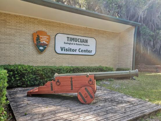 Exterior of the park's visitor center where another old cannon is on display, beneath the National Park Service's shield.