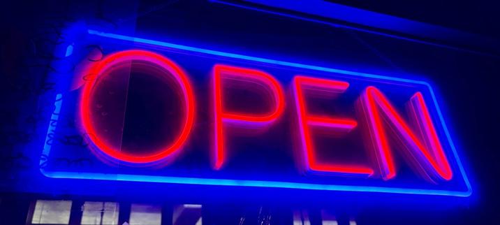 A vibrant blue and red neon "open" sign inside of a restaurant’s window, shot at night.