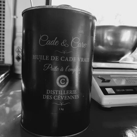 Un flacon d'huile de Cade des Cévennes, étiquette très chic, posé devant une balance de précision.