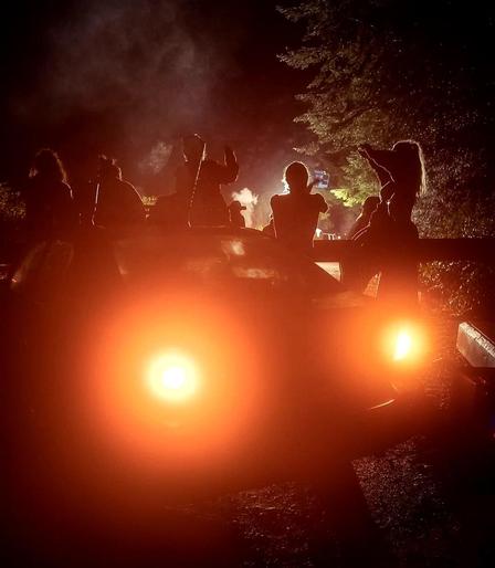 Activists blocking road in middle of night, facing off RCMP CIRG. Bright headlights light the scene.