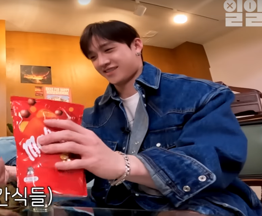 Bang Chan as seen through a fish-eye lens, from a low angle. On his left wrist he is wearing the Chrome Hearts flower cross curb chain bracelet.