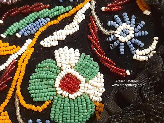 Detail of a rocaille embroidery on a black bonnet. Green, red, orange, blue and white beads form flowers. The stitching in parallel rows reminds of the ancient perlage technique used for 3-D flowers in the 19th century wreaths for the dead. This bonnet is a reconstruction made with modern glass rocailles.