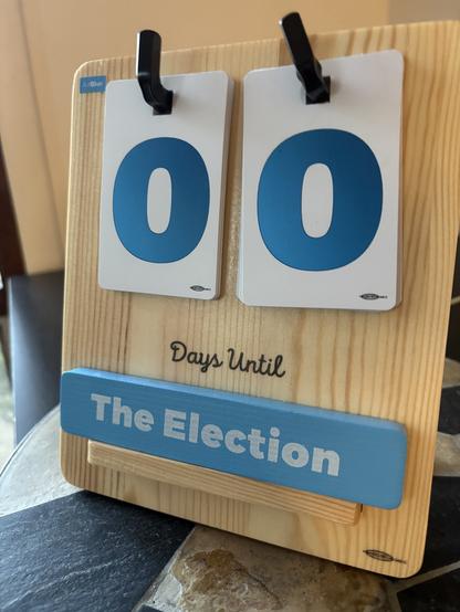 Countdown board showing "0 Days Until The Election" with blue numbers on white cards and a wooden base.
