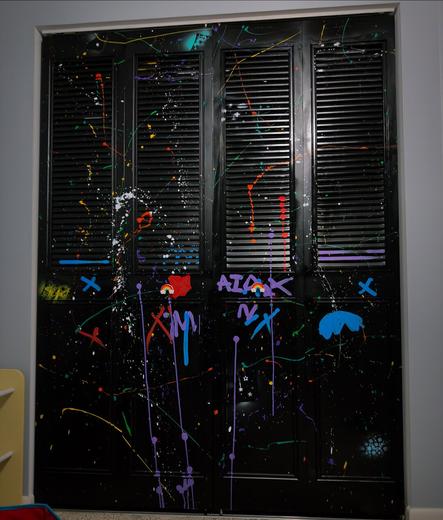 Folding and sliding closet door painted black and covered in splatter paint and graffiti markers.