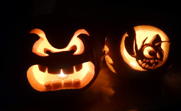 photo of two jack-o-lanterns in the dark - each carved pumpkin has a candle inside that illuminates the carved design - the pumpkin on the left is the face of a Thwomp from Mario and the pumpkin on the right is a silhouette of Stitch from Lilo & Stitch
