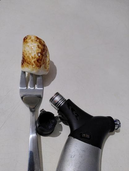 Kuchengabel mit gegrilltem Marshmallow, daneben ein Sturmfeuerzeug.
