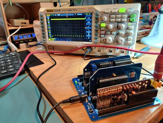 an RC2014 with a ZX81 module plugged in. an oscilloscope behind it has a signal showing stuff going on