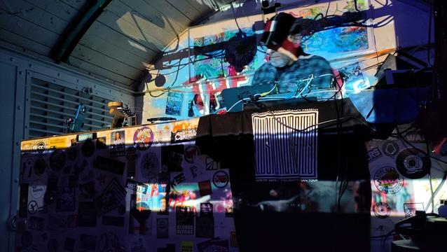 Ein elektronischer Liveact am DJ Pult des Waggon in Offenbach. Der Hintergrund ist durch einen Beamer bunt beleuchtet.