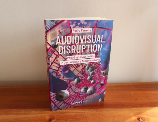 Book titled Audiovisual Disruption: Post-Digital Aesthetics in Contemporary Audiovisual Arts stands on a wooden surface.