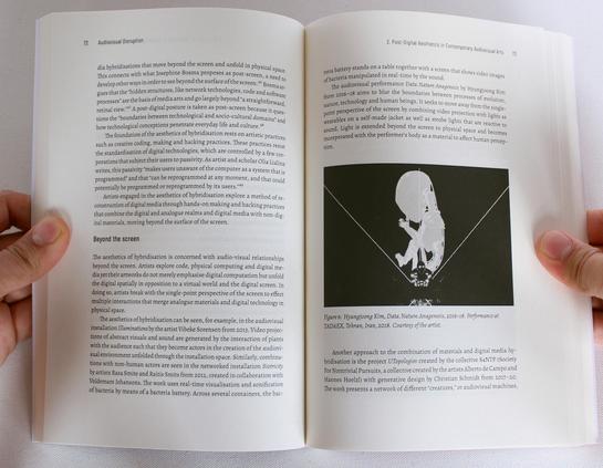 Hands hold a book open. The text header says "Beyond the Screen" and on the even page there is a photo of an AV Performance.