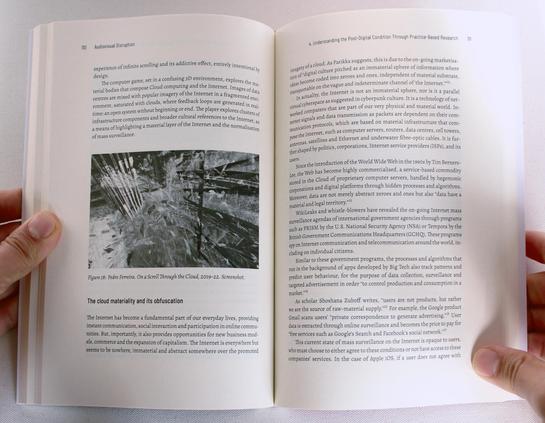 Hands hold a book open. The text header says "The cloud materiality and its obfuscation" and on the odd page there is a photo of a glitch image.