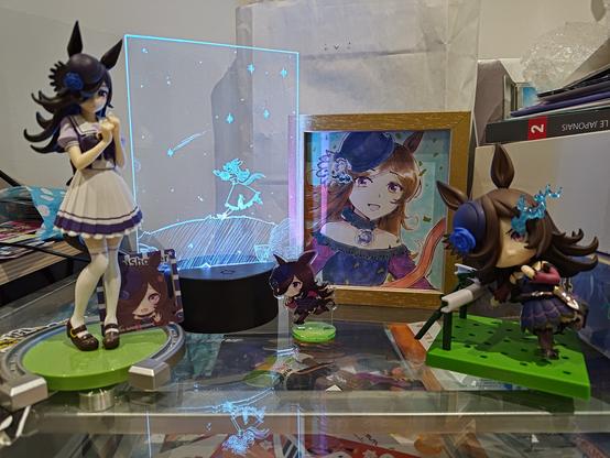 Une photo de mes différentes figurines de Rice Shower, entourant une le standee lumineux décrit juste avant, et une autre illustration de Rice Shower faite sur shikishi. Sur cette dernière, Rice paraît radieuse après avoir gagné une course