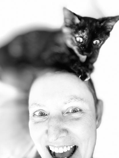 Black and white selfie with a wide-eyed tortoiseshell kitten on my head