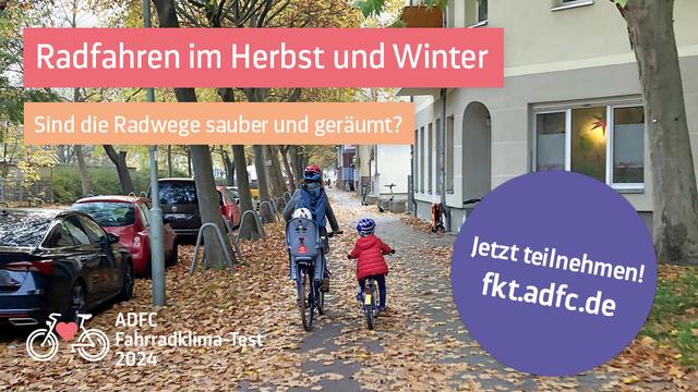 Familie auf Fahrrädern auf einem mit Laub bedeckten Radweg in einer Stadt zwischen parkenden Autos und einer Hausfassade.