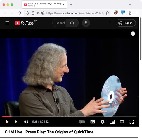 Screenshot of a Computer History Museum panel discussion YouTube video with members of the original QuickTime team. Current still frame: Peter Hoddie, older than pictured in the TI/99 hall of fame, holding up a 12" LaserDisc and smiling.