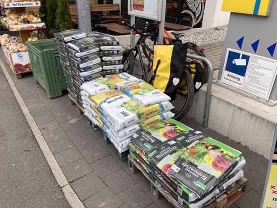 Mit Blumenerde zugestellt Fahrradständer. In der Lücke zwischen Erde und Ständer steht trotzdem ein Fahrad mit Packtaschen.