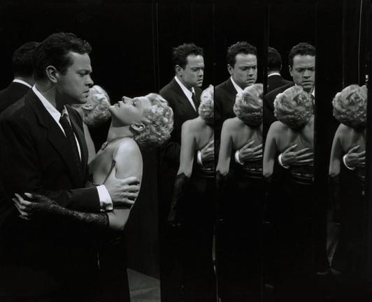 an iconic scene from the final reel of Lady From Shanghai, as Orson Welles holds Rita Hayworth in the Hall of Mirrors in a Fun House, their multiple reflections surrounding them.