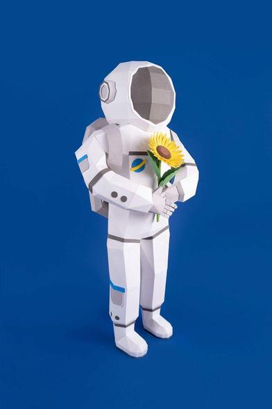 A papercraft astronaut holding a sunflower against a blue background.
