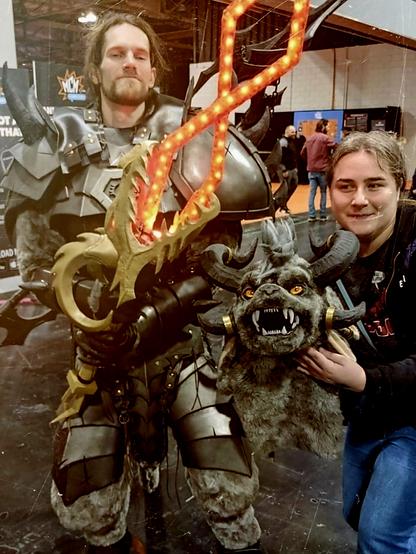 Myself cosplaying as a Charr (large armoured hellcat) from Guild Wars 2, holding an LED flaming sword. Costume Head is being held beside me by my ever supportive Mrs.