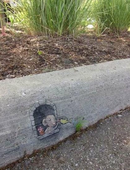A photograph of a concrete curb, maybe a foot high above which is soil and grassy plants. At the foot of the curb is a tiny grassy plant, in green.

Drawn on the curb is a window with a flowerpot
A cartoon mouse is drawn with a yellow watering can, apparently watering the tiny grassy plant just below