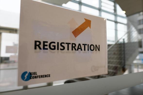 A sign reading “Registration” hangs on a glass stairwell door. In one corner of the sign is the Kiel Conference logo