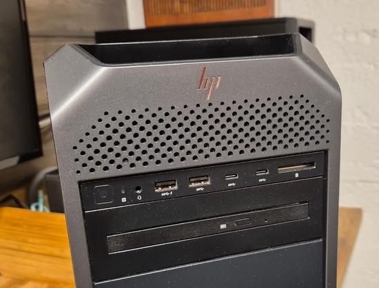 A closeup of the HP logo on the front panel of a Z4 workstation, it sits over a perforated area with small round holes. Beneath that is a row of connectors and the 5.25 inch bays. The case has cut corners, which makes for an interesting shape.