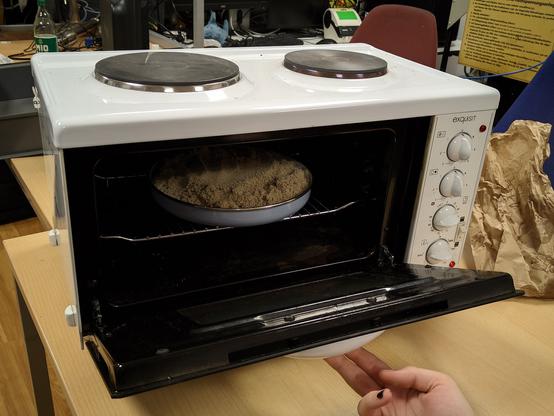 A microwave microwaving a pan of sand at 250°C