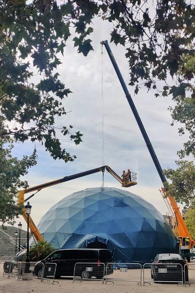 Unas grúas amarillas montan un domo gigante en la explanada del palacio de Congresos. Unas personas con casco están subidas en el cestillo de una de las grúas.