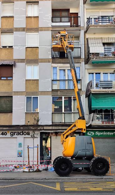 Unos pintores subidos en una grúa amarilla pintan la fachada de un edificio en la Avda. de Dílar.