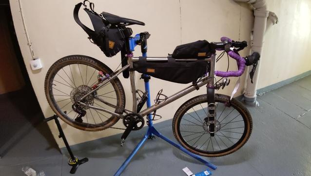 Vélo gravel en titane avec sa bagagerie sur un pied d'atelier