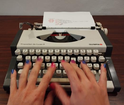 I'm typing on a Olympia Traveller de Luxe S. My nails are painted in the colors of the bisexual flag.