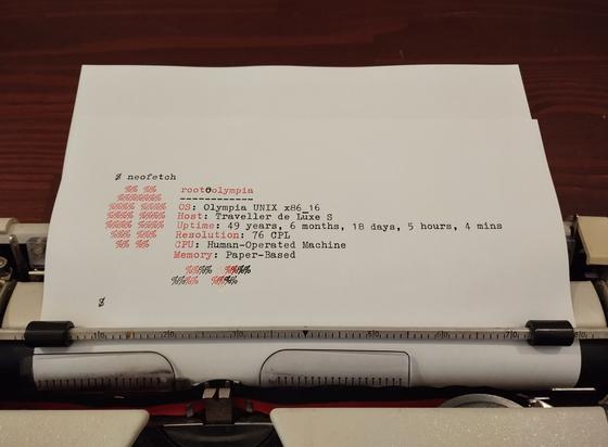A photo of the sheet of paper I was typing on in the previous photo. A fake Neofetch output has been painstakingly typed on it:
- The user and the host are root@olympia;
- The OS shows up as Olympia UNIX x86_16;
- Its host is Traveller de Luxe S;
- The uptime is 49 years, 6 months, 18 days, 5 hours, 4 mins
- The resolution is 76 CPL
- The CPU field says Human-Operated machine
- The memory is Paper-Based
