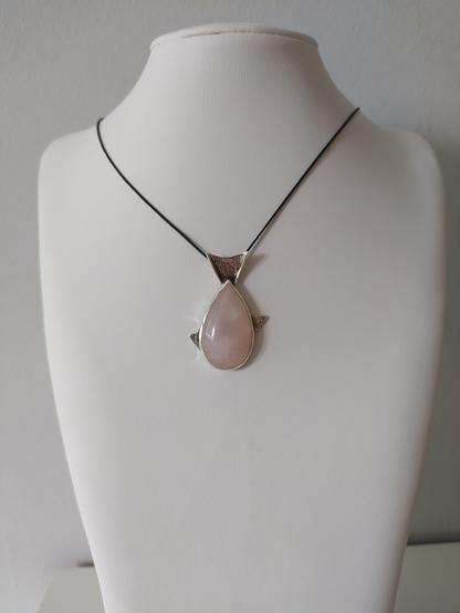 a fish shaped silver pendant with a teardop shaped pink gemstone as the main body of the fish. it has a black cord